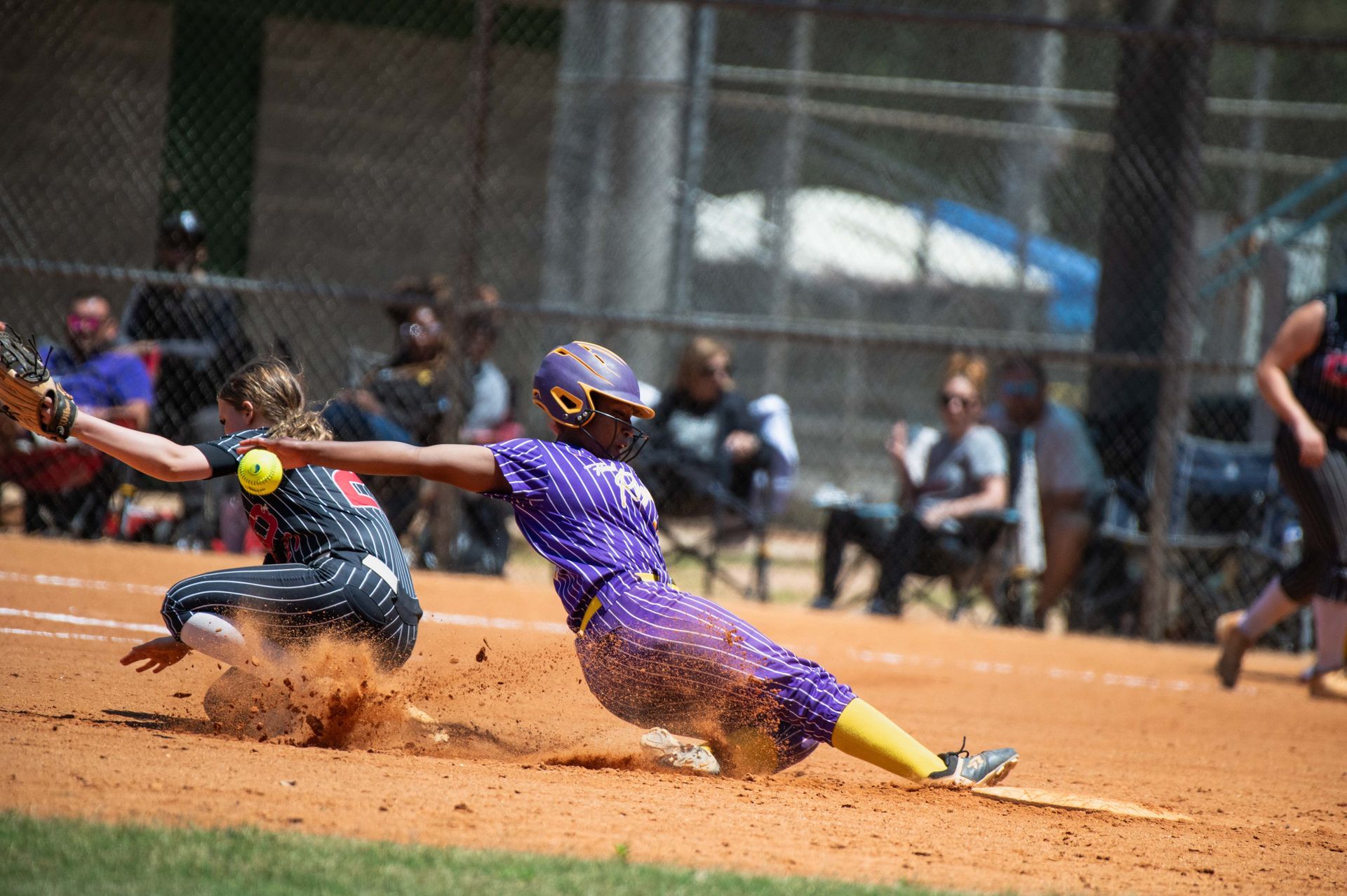 Two softball players slide into a dusty base during a close play on the field