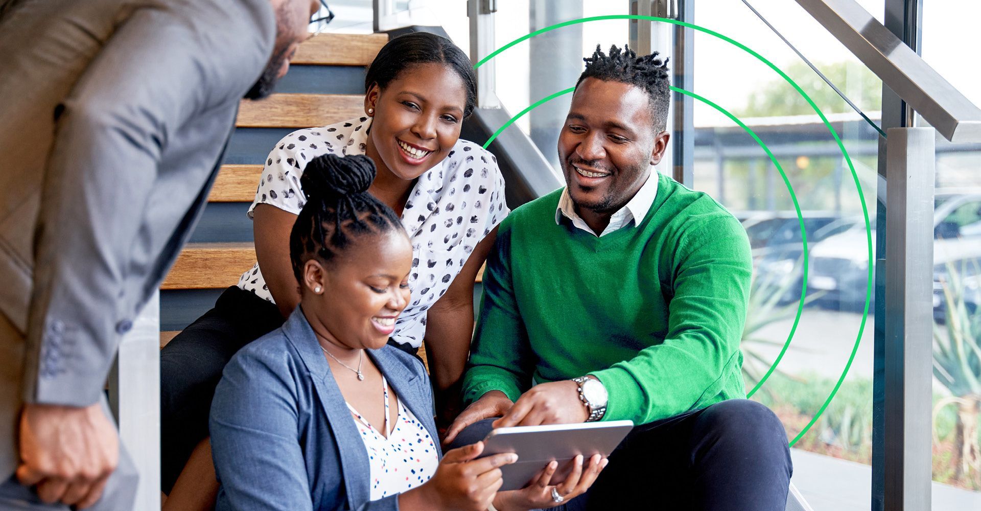 Group of smartly dressed happy people sitting on stairs looking at a tablet