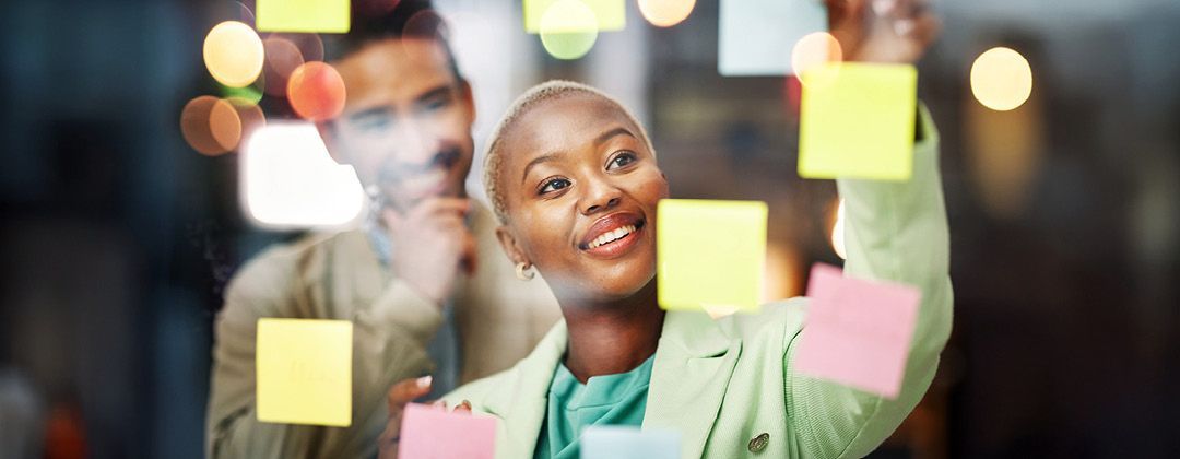 Lady standing next to a project board with sticky notes.