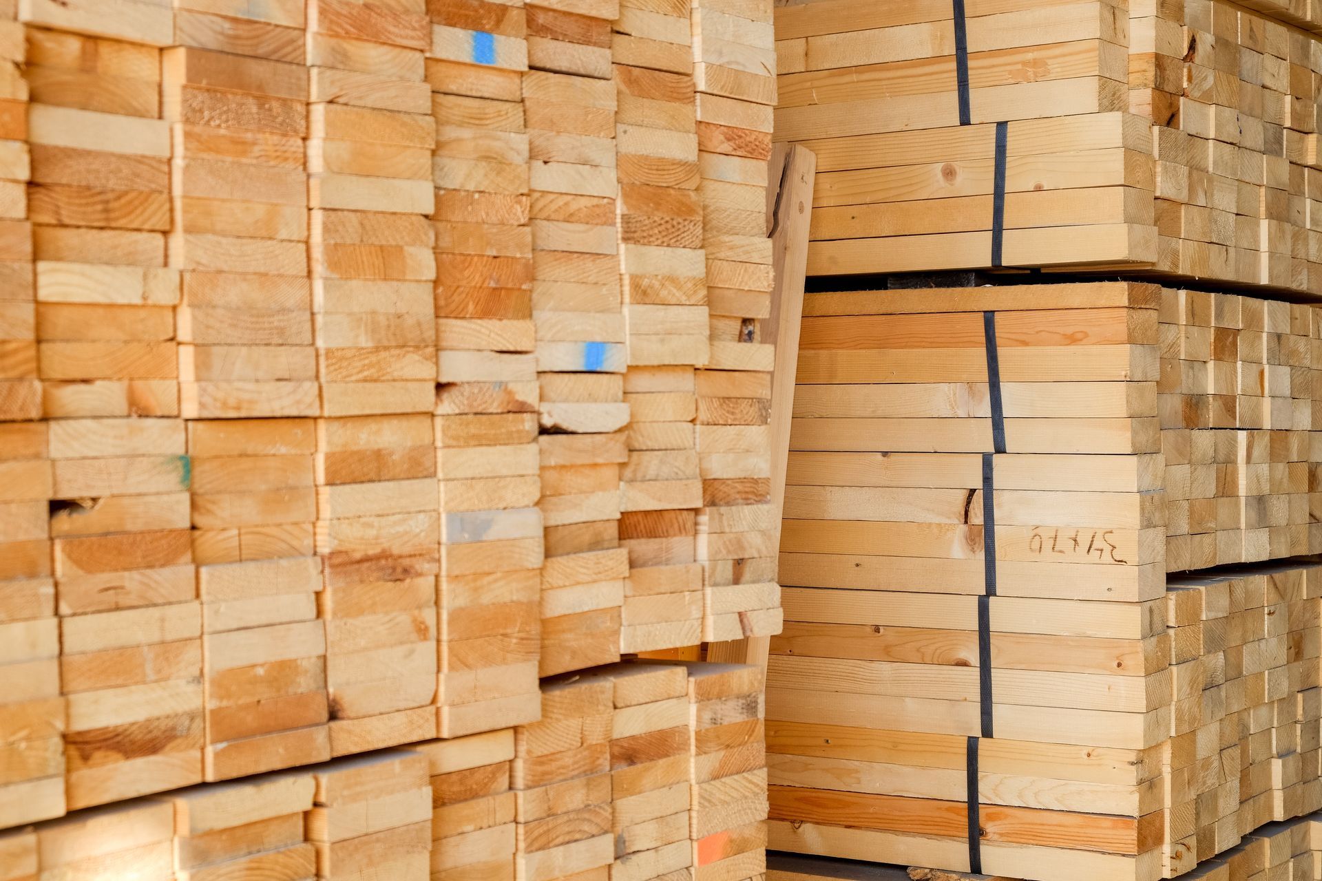 Stacks of light brown wooden boards piled in a lumberyard or storage area.