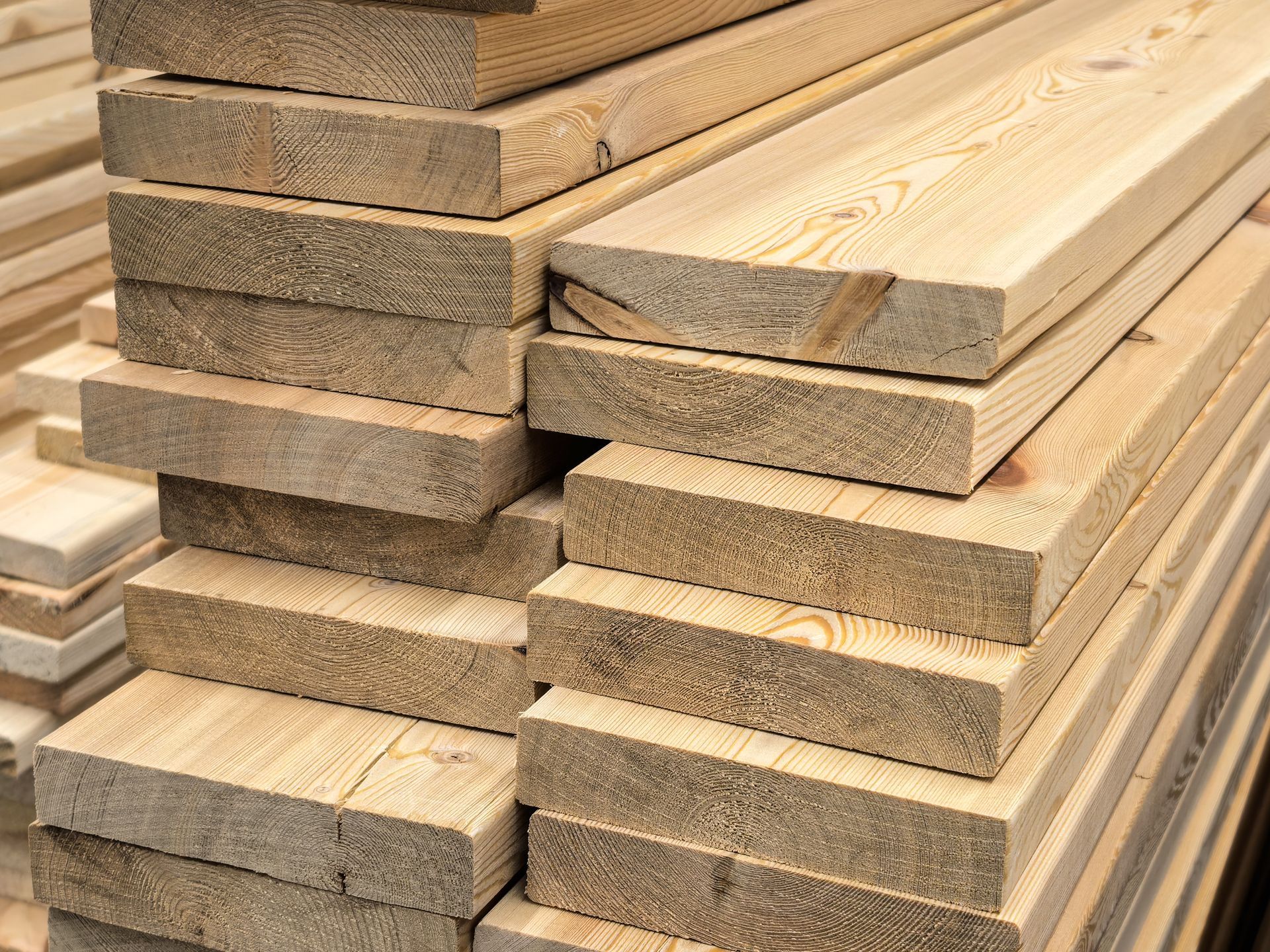 Stacks of light-colored lumber boards piled in a workshop or lumberyard.