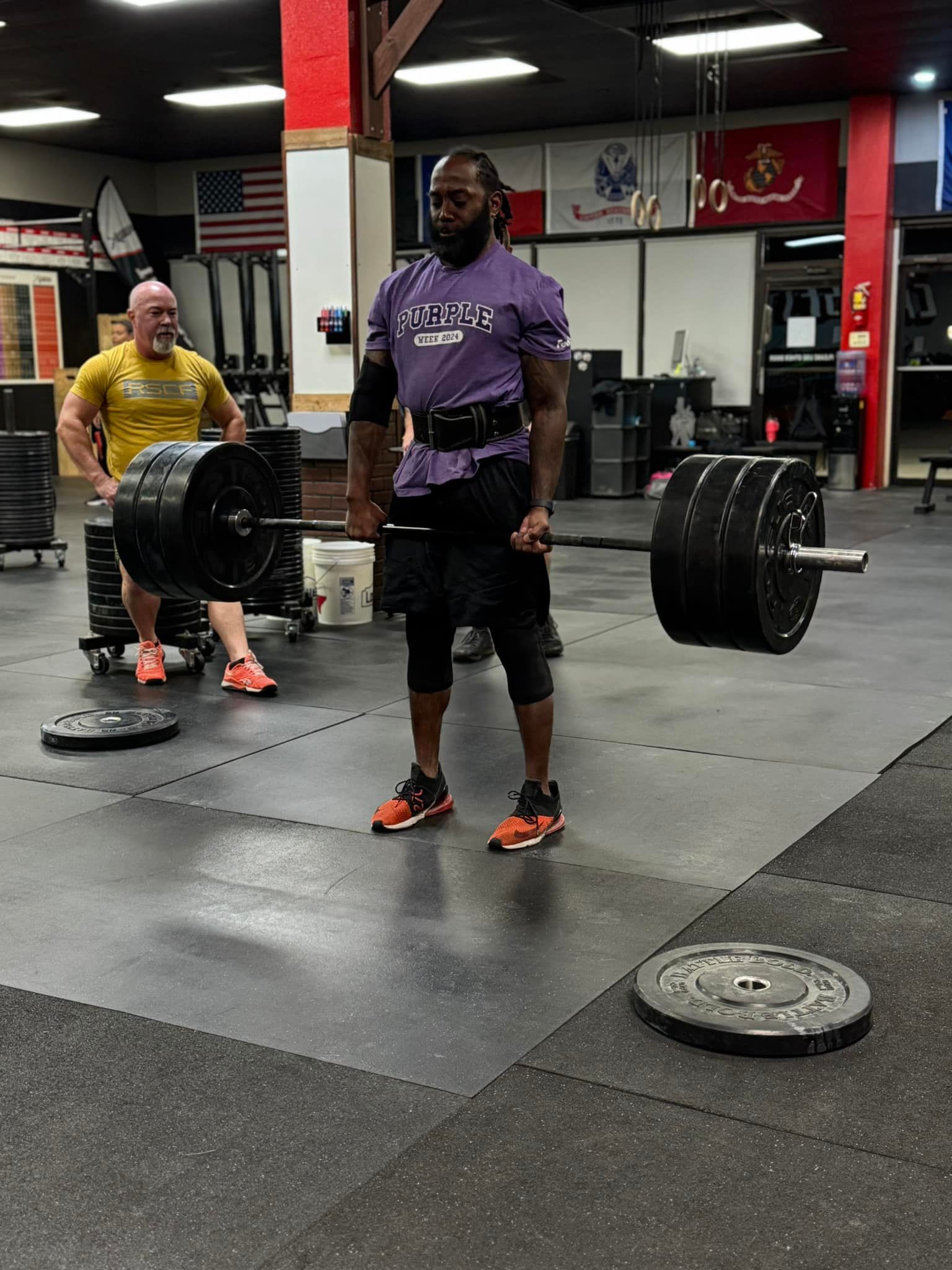 A man in a purple shirt is holding a barbell in a gym.