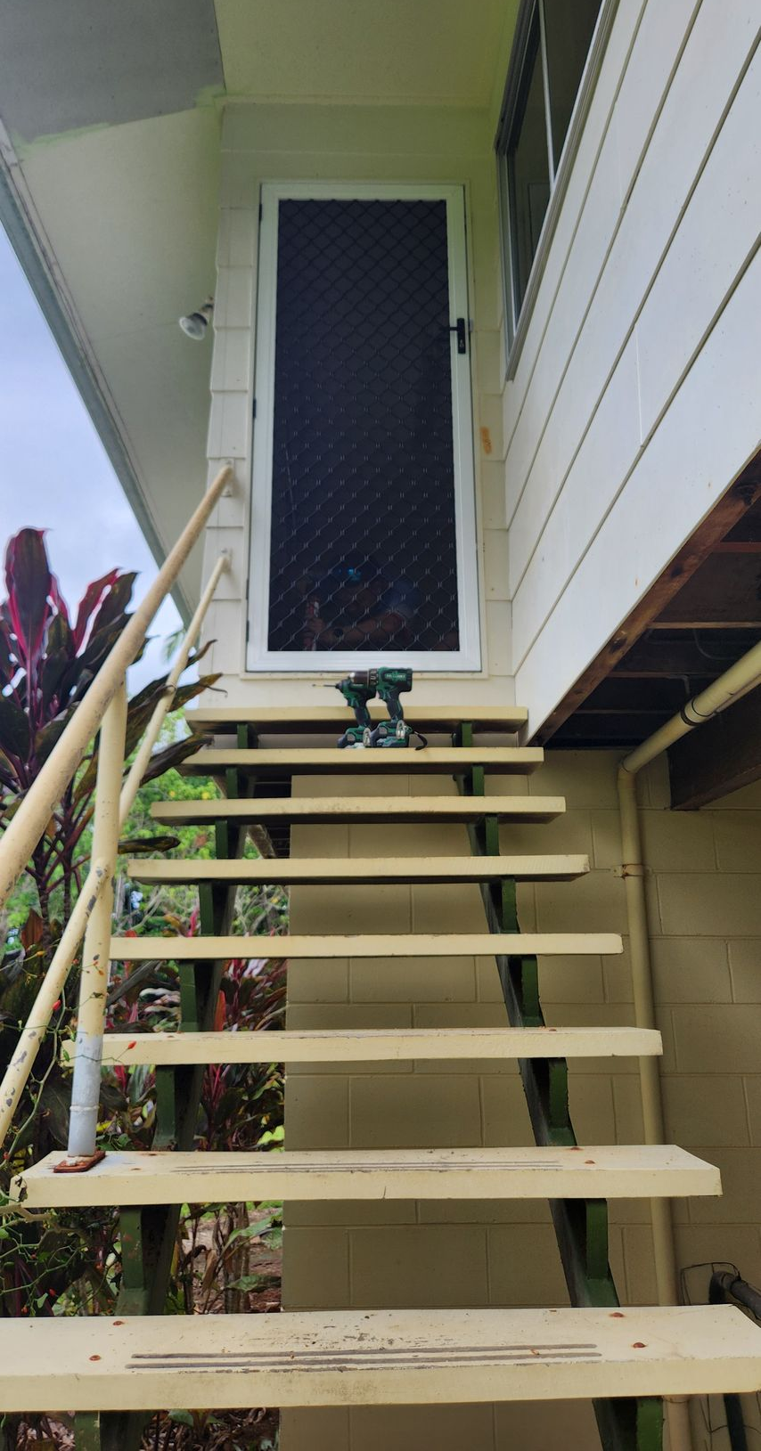 Staircase leading to a screened door. A drill sits on the stairs. White house siding.- Advancetech Glass & Glazing in Wulguru, QLD