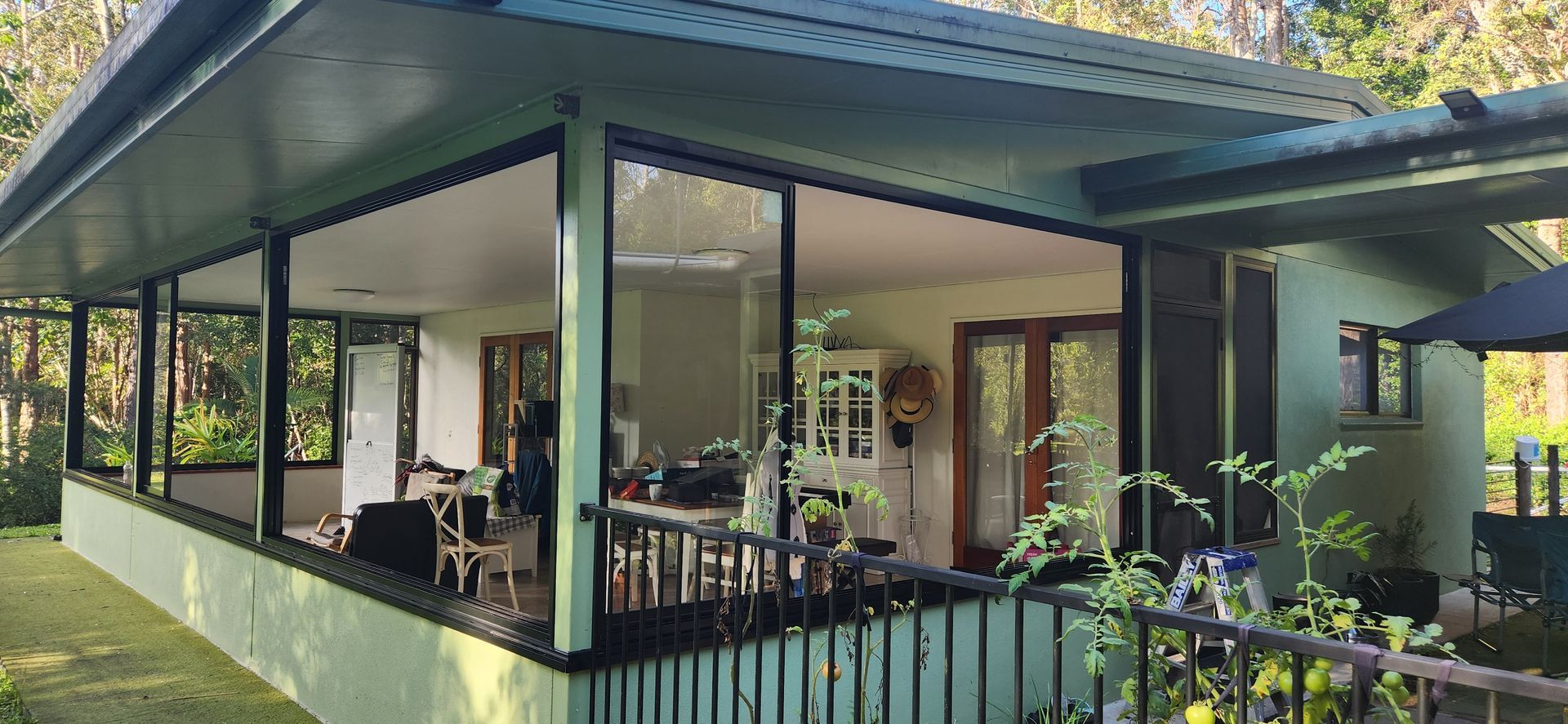 A green house with large windows and a porch, surrounded by greenery - Advancetech Glass & Glazing in Wulguru, QLD