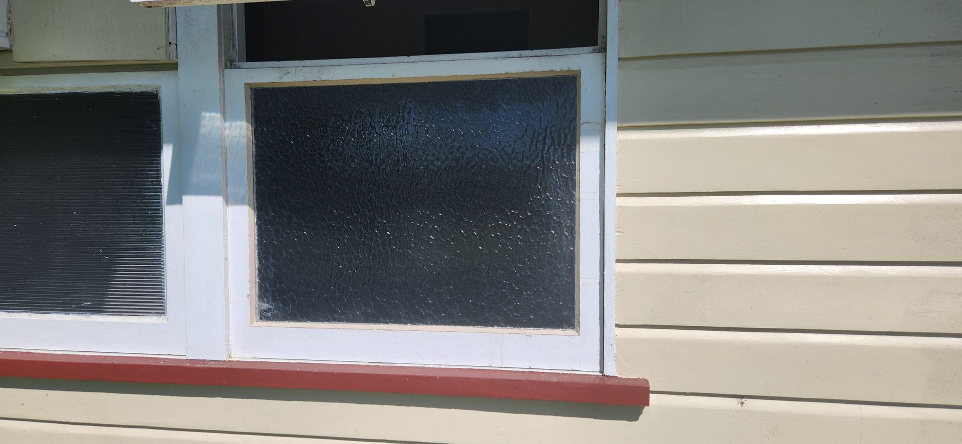 Window on a cream-colored building with a red trim. The window panes are dark — Advancetech Glass & Glazing in Wulguru, QLD