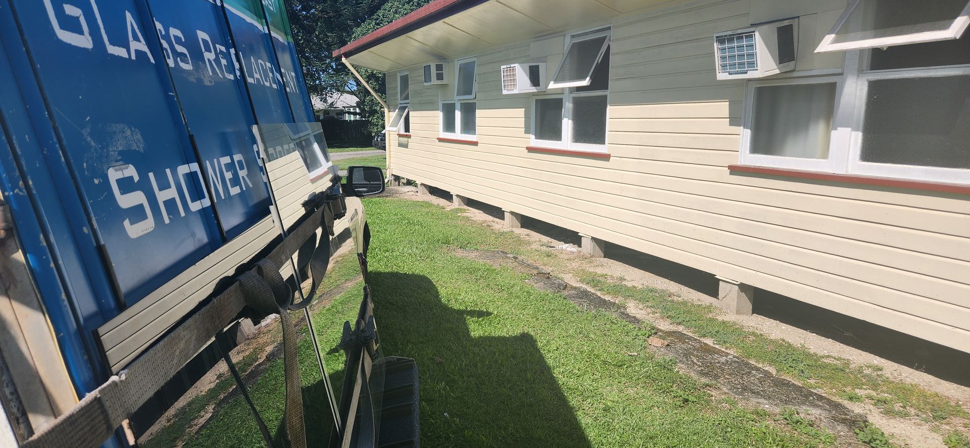 Blue glass sheets in a truck next to a beige building with windows and air conditioners. Green grass — Advancetech Glass & Glazing in Wulguru, QLD