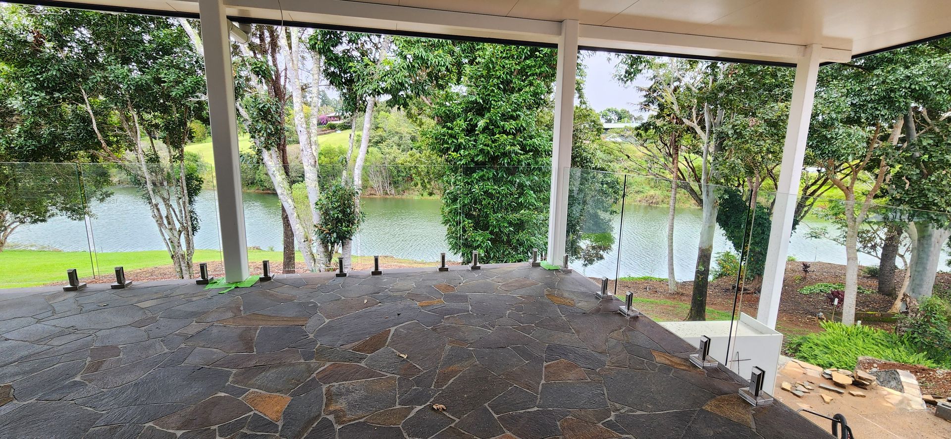 Covered patio overlooking a river, framed by white columns, and green trees Advancetech Glass & Glazing in Wulguru, QLD