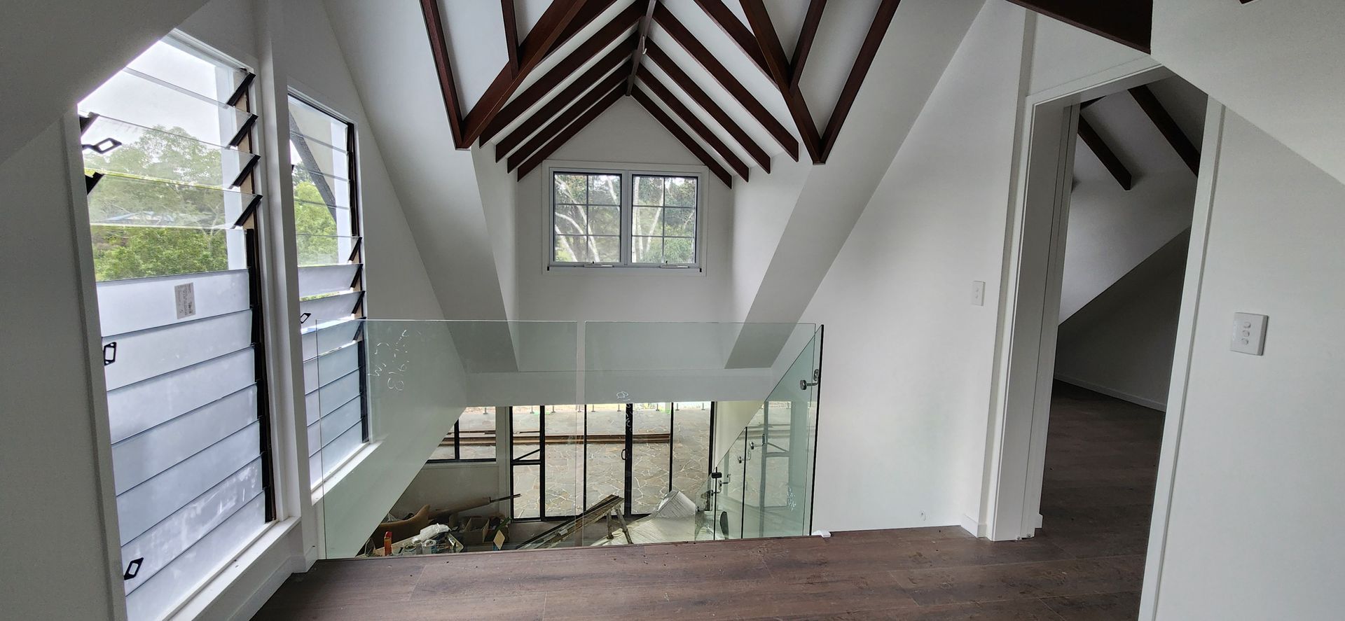Interior of a room with a pitched ceiling, dark wooden beams, a window, and white walls — Advancetech Glass & Glazing in Wulguru, QLD
