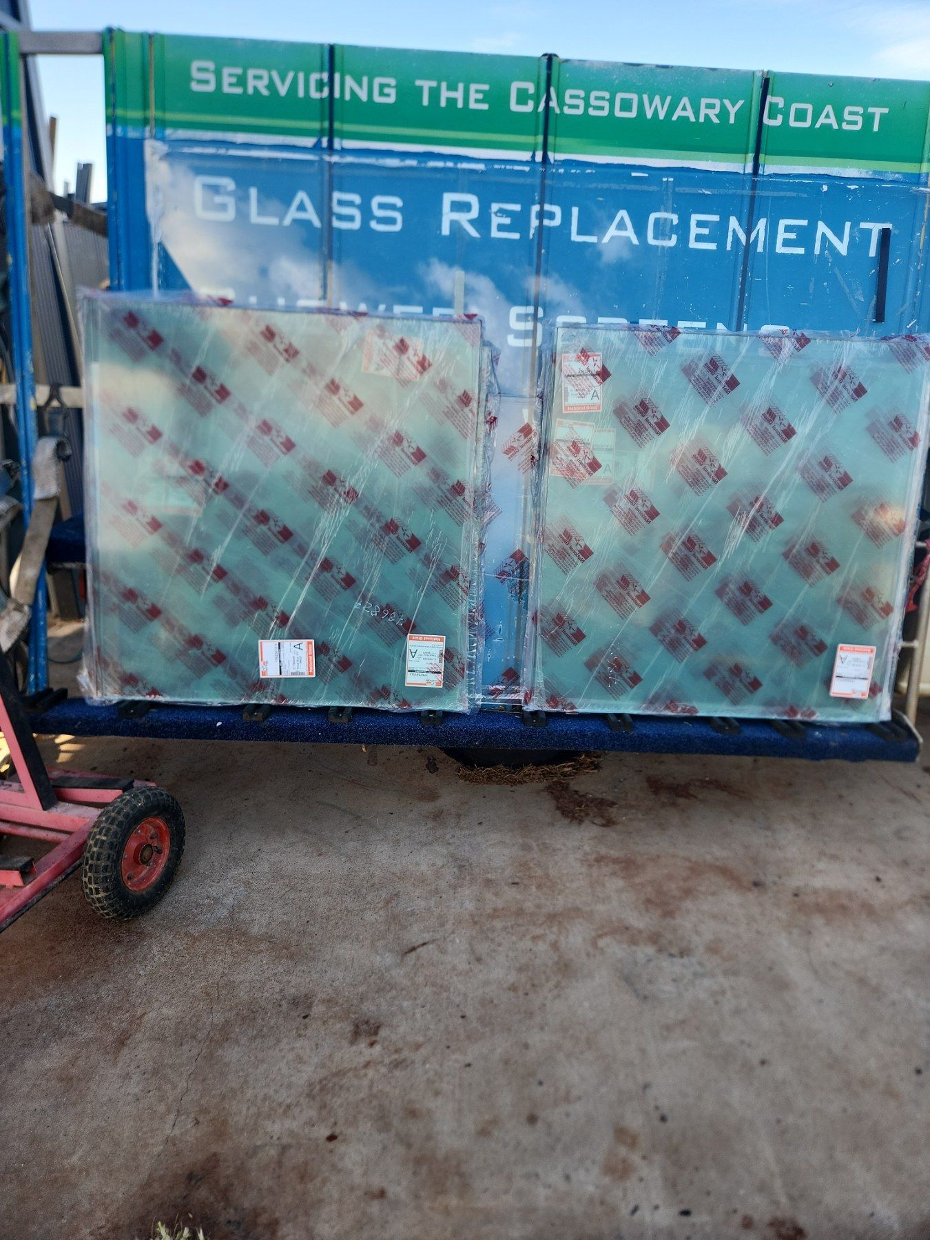 Two wrapped glass panes on a cart, ready for glass replacement service. Signage reads