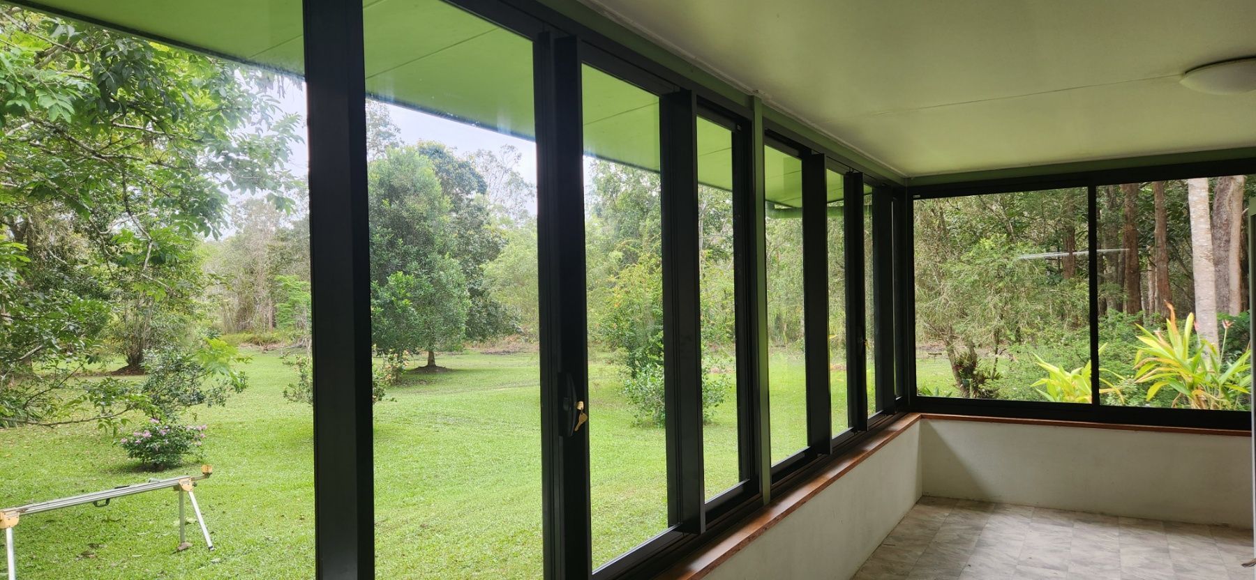 Indoor view of a room with large windows overlooking a yard with trees and a truck parked outside - Advancetech Glass & Glazing in Wulguru, QLD