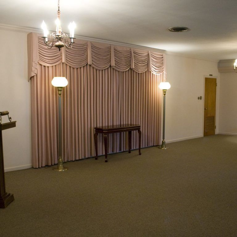 Empty room with pink drapes, two standing lamps, a small table, and a closed wooden door
