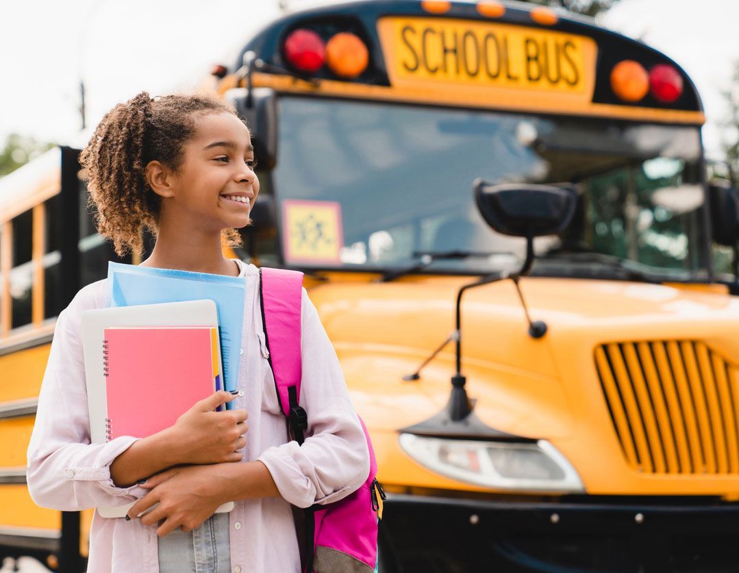 girl teenager pupil student preparing to go to school after summer holidays holding books and notebooks standing next to the school bus