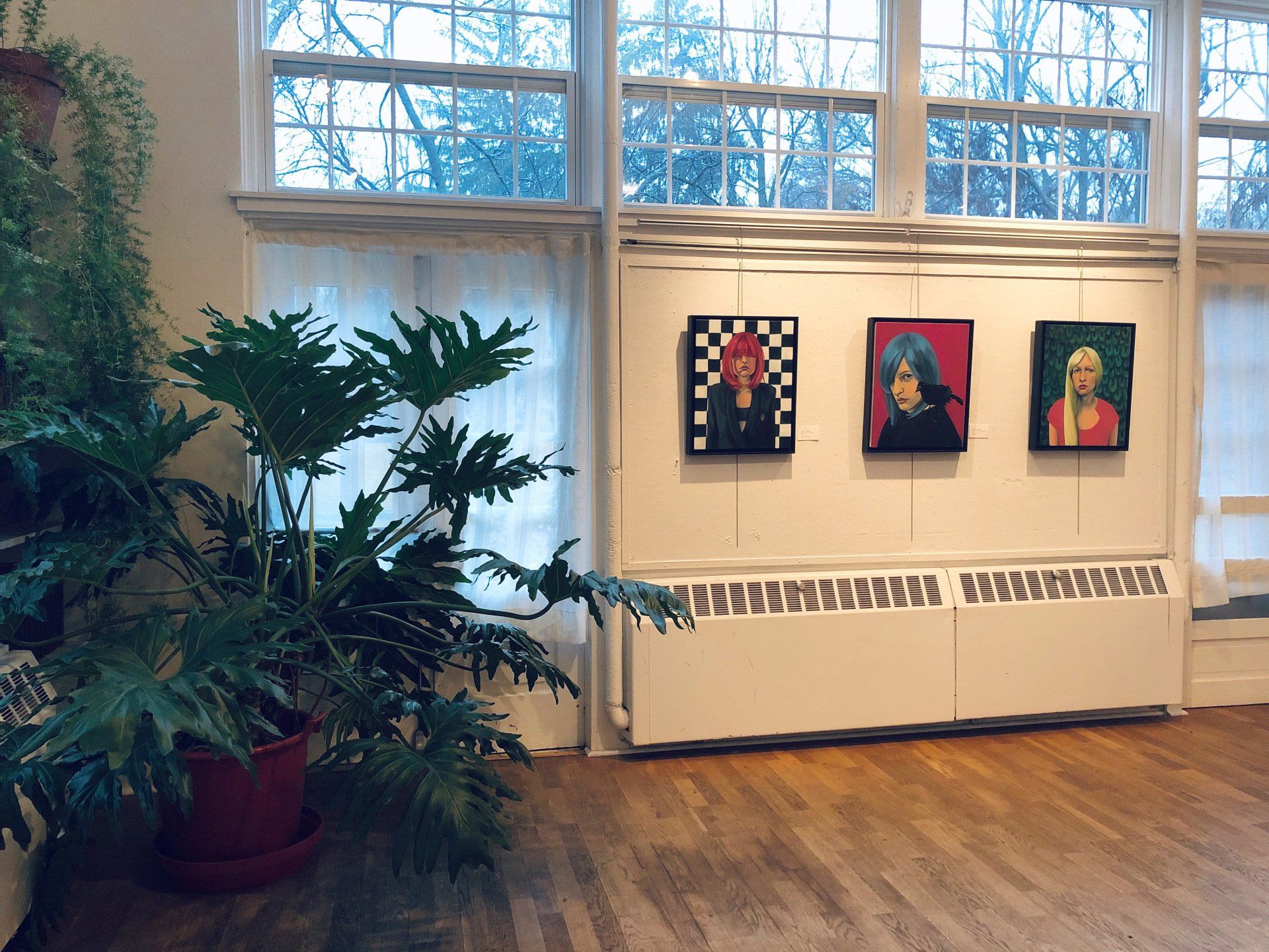 Three paintings on a wall with many windows and a large plant, Arden Buzz Ware Center 2019