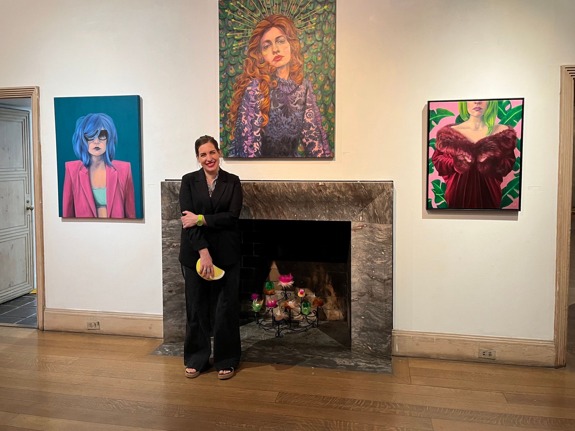 The artist in front of a fireplace and three paintings hanging around it, Abington Art Center 2023