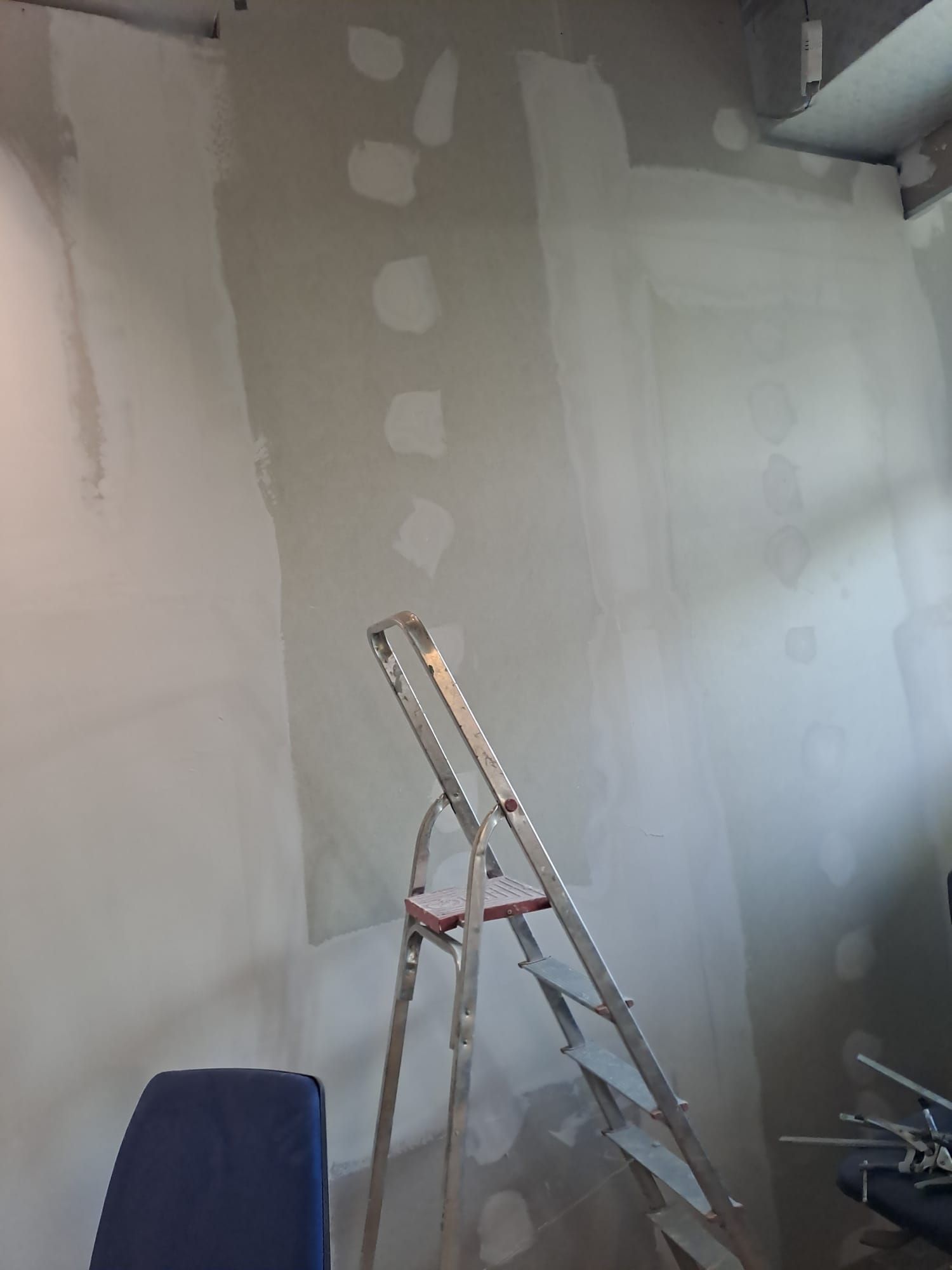 Scala in una stanza con pareti grigie e bianche appena intonacate e riparazioni in cartongesso a chiazze
