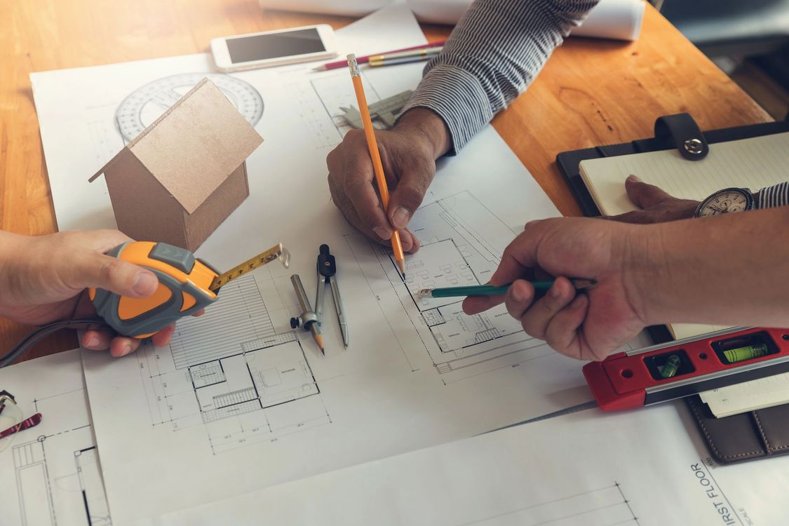 Mani che disegnano la pianta di una casa con attrezzi e strumenti di misurazione su un tavolo