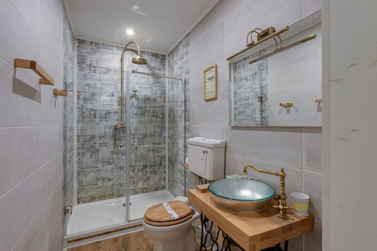 Bagno moderno con doccia in vetro, specchio a parete e mobile in legno con lavabo in rame.