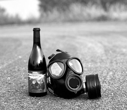 Wine bottle and gas mask resting on pavement with trees in the background.