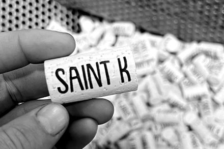 Close-up of crushed grape clusters in the crusher bin during aHand holding a cork branded SAINT K over a pile of corks.harvest processing.