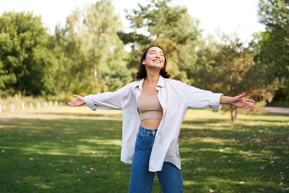 a woman is standing in a park with her arms outstretched .