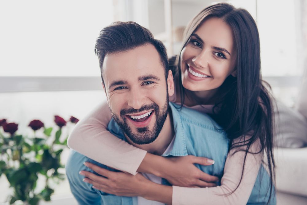 a man is giving a woman a piggyback ride and they are smiling for the camera .