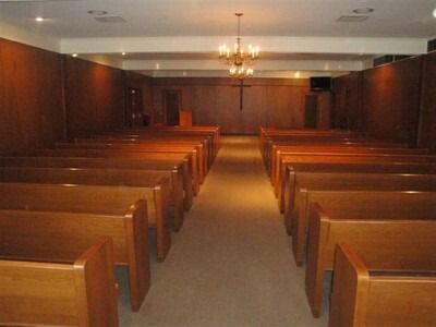 Empty wooden church pews facing a pulpit in a dimly lit chapel