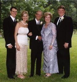 Five people dressed formally standing together outdoors on a lawn.