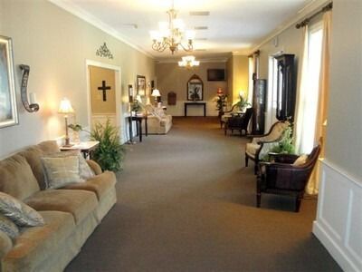 Long carpeted hallway with beige sofas, chairs, wall art, and chandeliers in a bright room