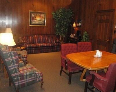 Cozy lounge with plaid armchairs, red chairs, a wooden table, lamp, and couch in a wood-paneled room