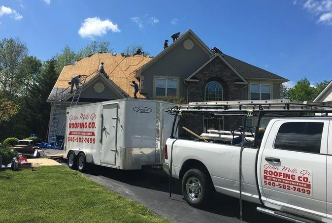 Roofing crew working on a house with a trailer and truck parked in the driveway.