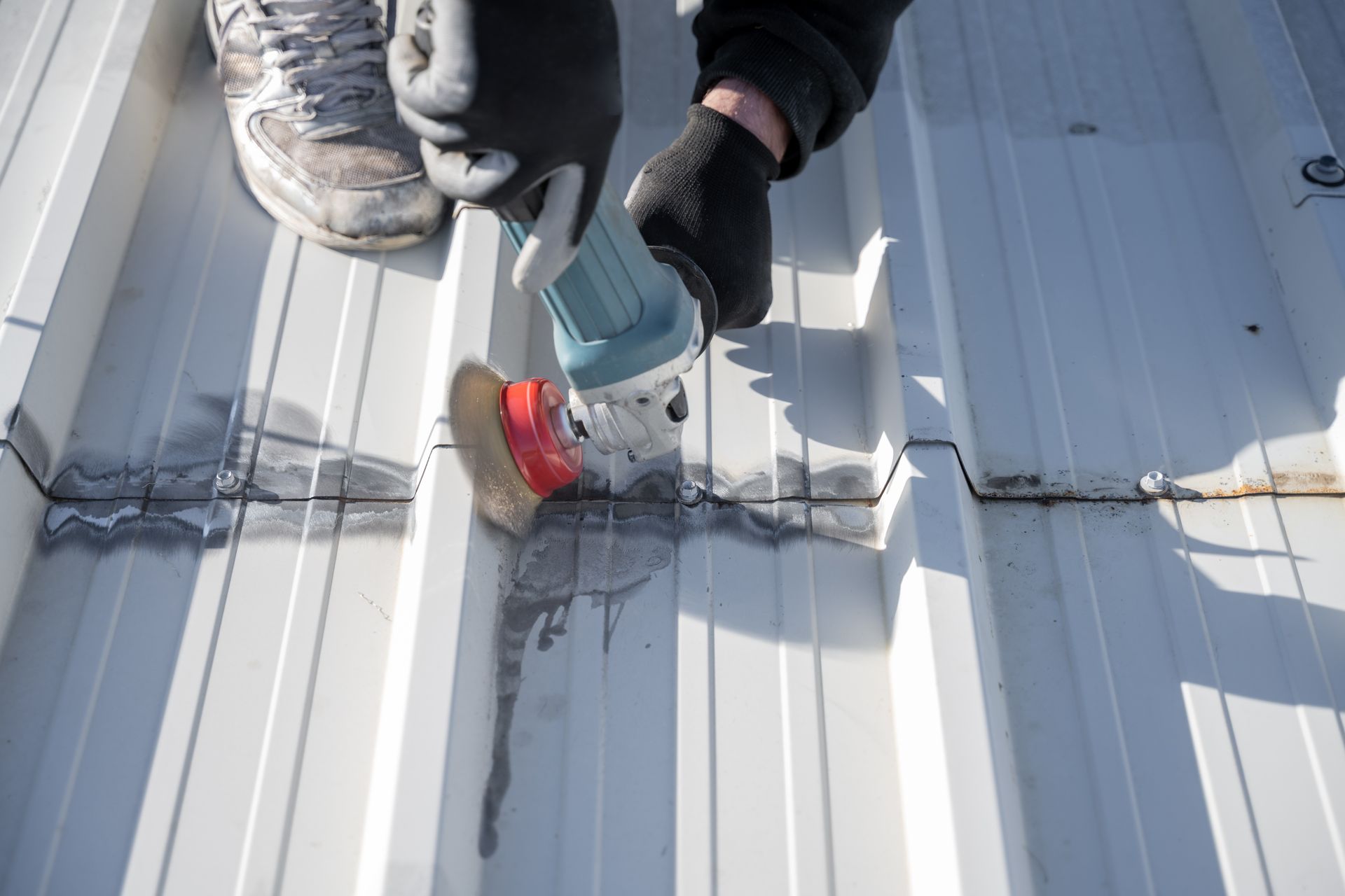 Worker using a power tool to grind and clean seams on a metal roof, preparing the surface.