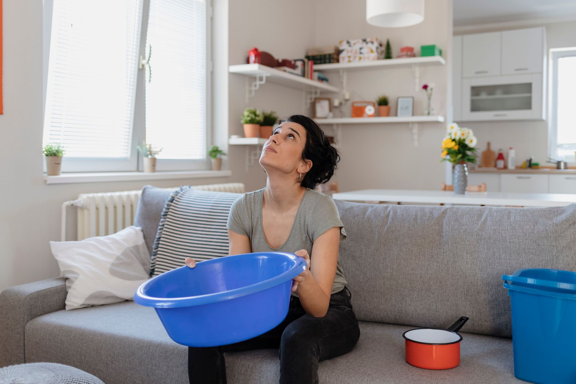 Person with blue basin on couch in modern living room, kitchen in background, cozy home interior.