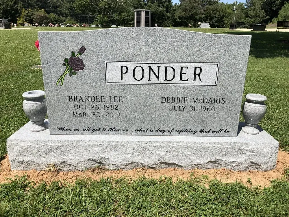 Gray granite memorial bench engraved “PONDER” in a cemetery, with small vases on either side.