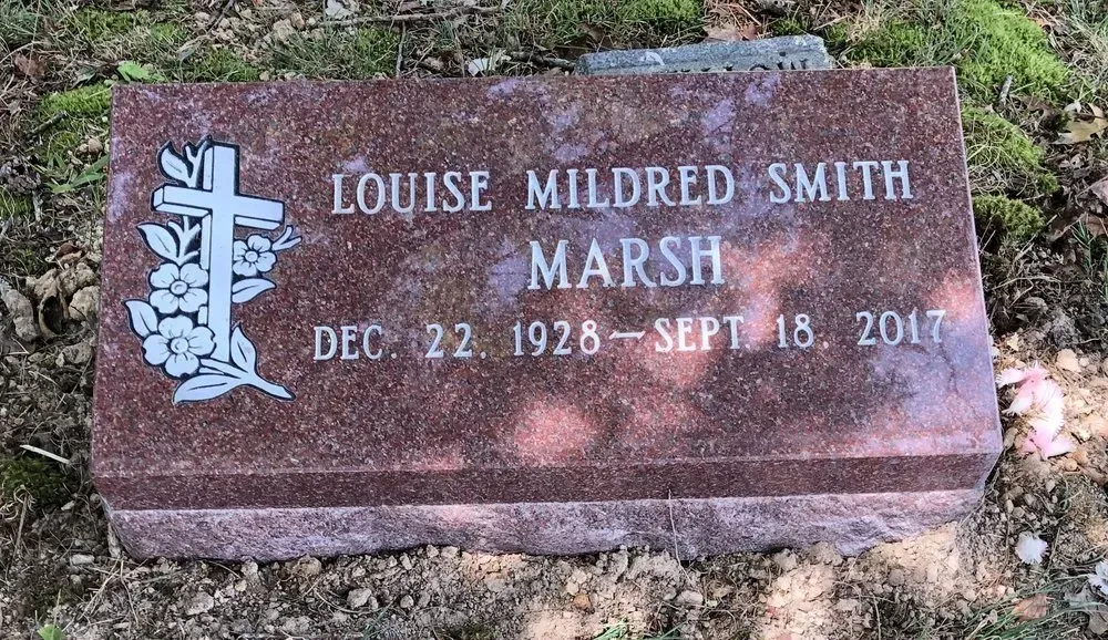 Gravestone for Louise Mildred Smith Marsh, reddish-brown stone with cross emblem in grass.