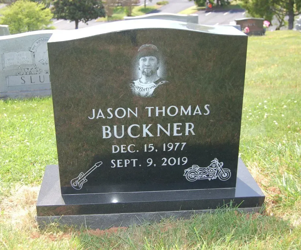 Black gravestone for Jason Thomas Buckner with etched portrait in a grassy cemetery.