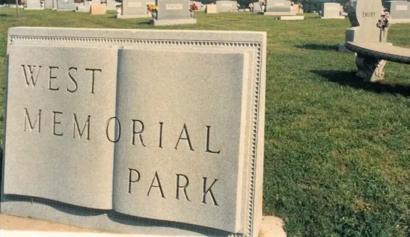 Stone sign reading “West Memorial Park” on a grassy lawn.