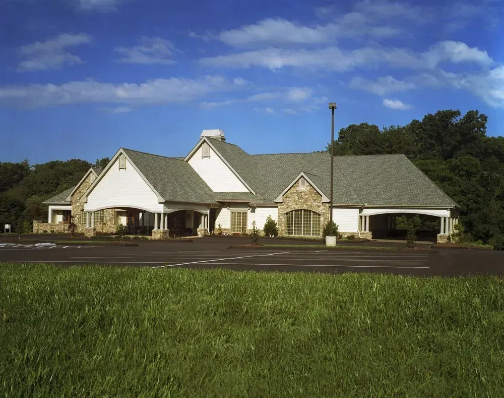 Single-story white building with green roof beside a parking lot under a blue sky