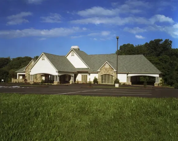 Single-story white building with green roof beside a parking lot under a blue sky