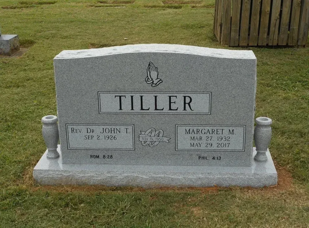 Gray gravestone engraved “TILLER” in a grassy cemetery, with two smaller name plaques and angel accents