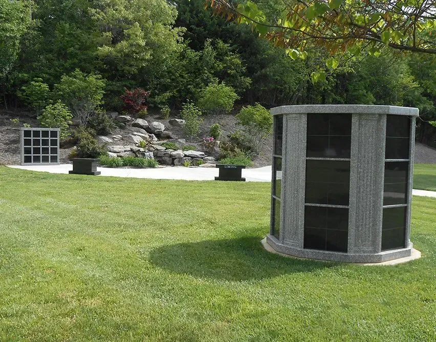 Curved stone memorial wall with plaques on a grassy lawn in a landscaped park