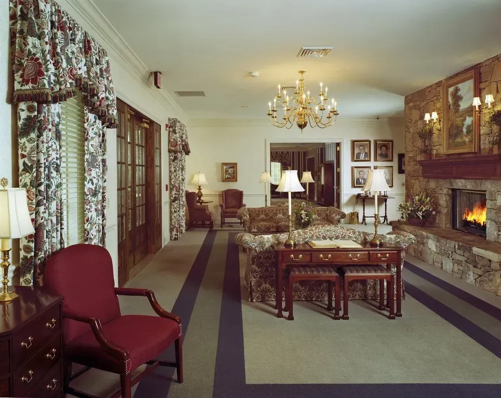 Elegant living room with chandelier, fireplace, patterned carpet, red chair, and large windows