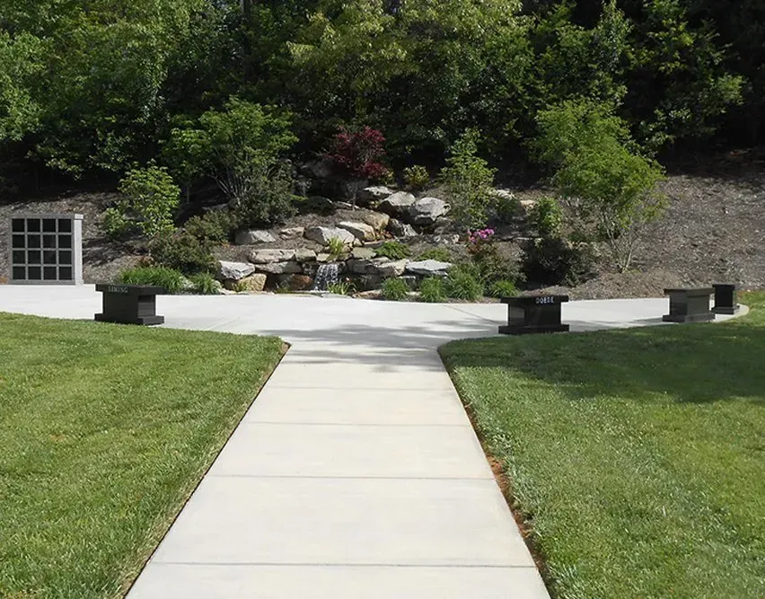 Concrete walkway leading to a landscaped garden with rocks, shrubs, and green lawn on both sides