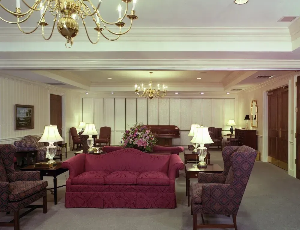 Elegant hotel lobby with a burgundy sofa, armchairs, chandeliers, and lamps in a spacious cream-toned room