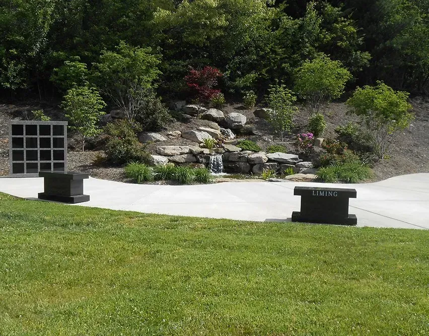 Landscaped garden with rocks, shrubs, and a concrete path beside a grassy lawn.