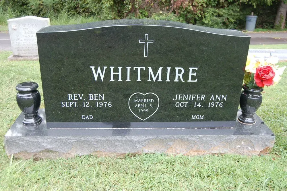 Whitmore gravestone with cross, names and dates, black stone with flowers in a cemetery