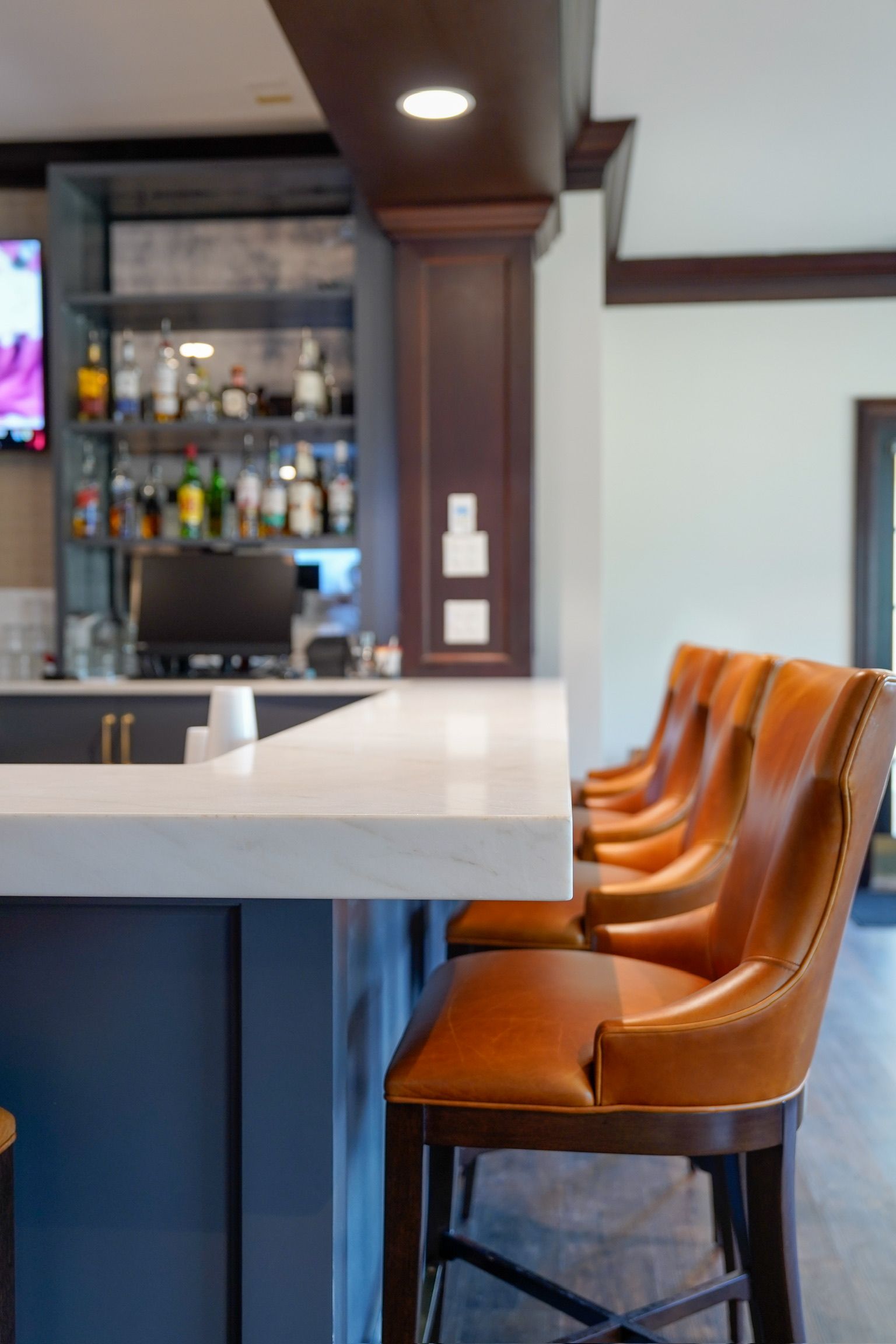 A bar counter with white stone surfaces, dark blue cabinets, and a row of tan leather bar stools.