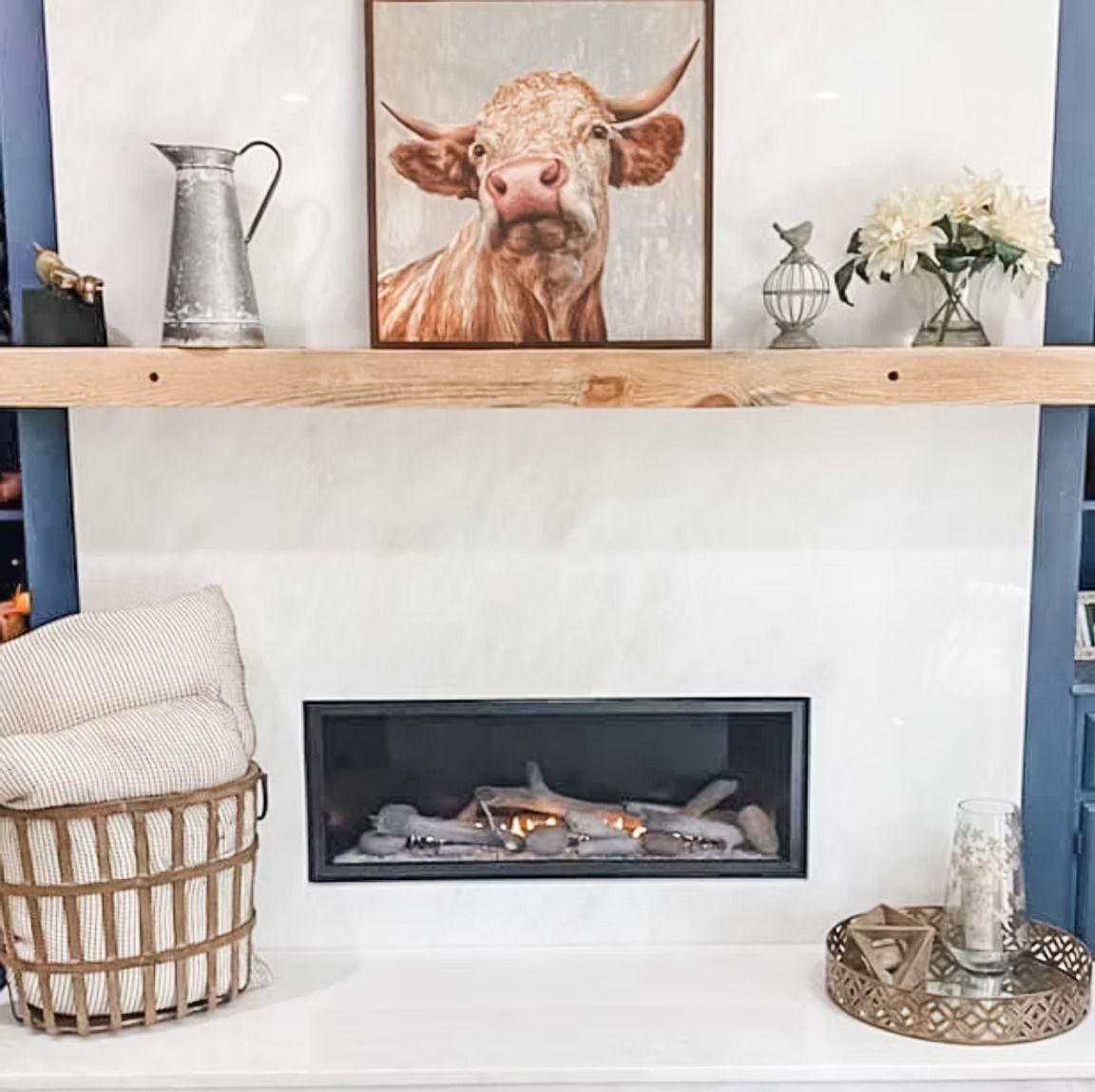 White fireplace with cow artwork, flowers, and decorative items.