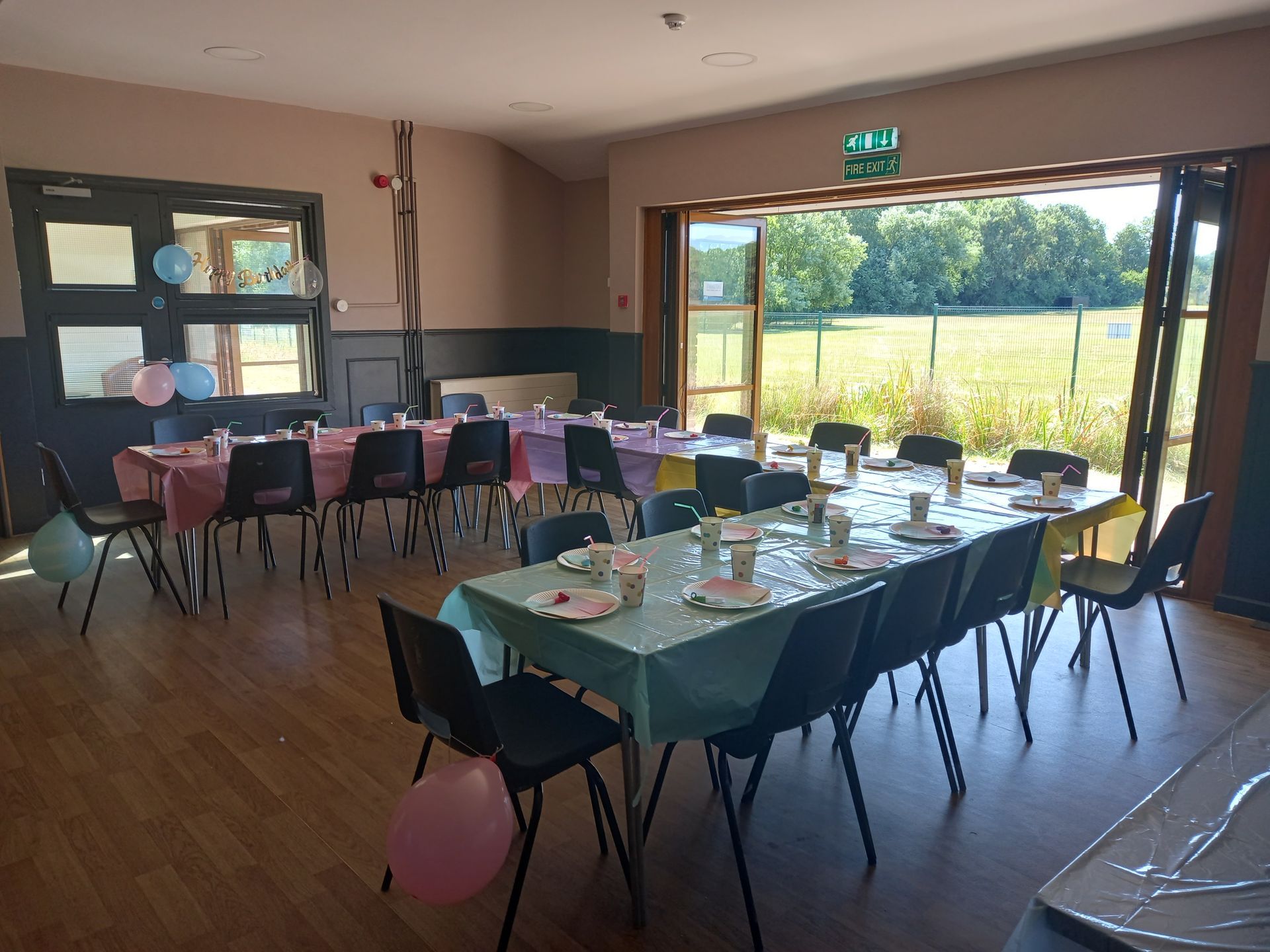 Empty banquet hall with set tables, chairs, and a large open doorway overlooking greenery