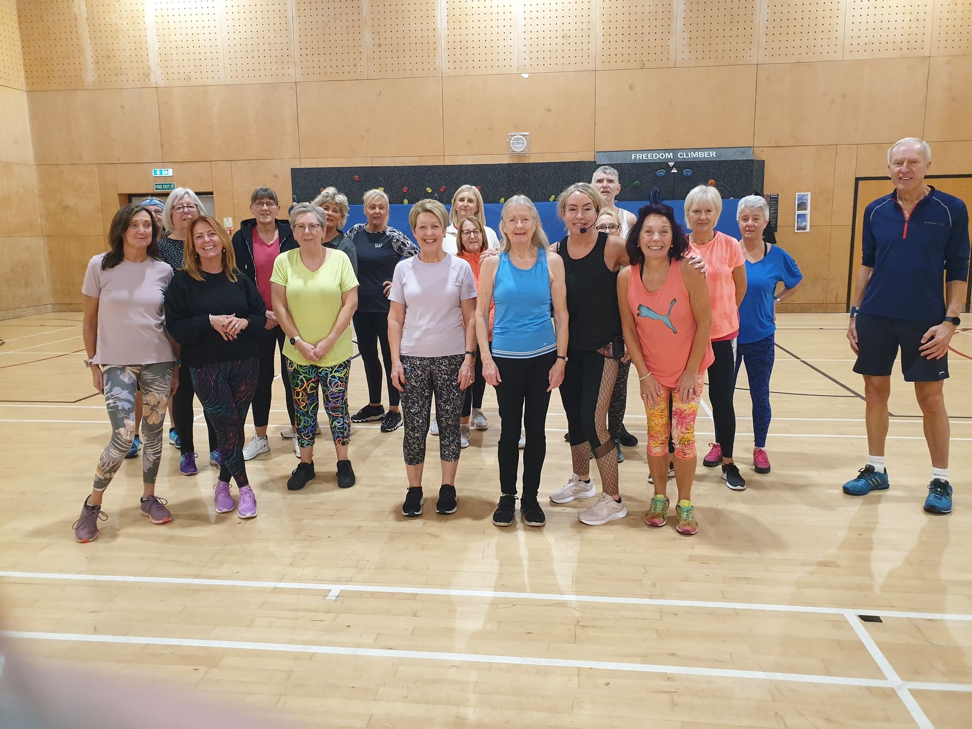 Group of people standing in a gymnasium, posing in workout clothes with basketball courts in the background