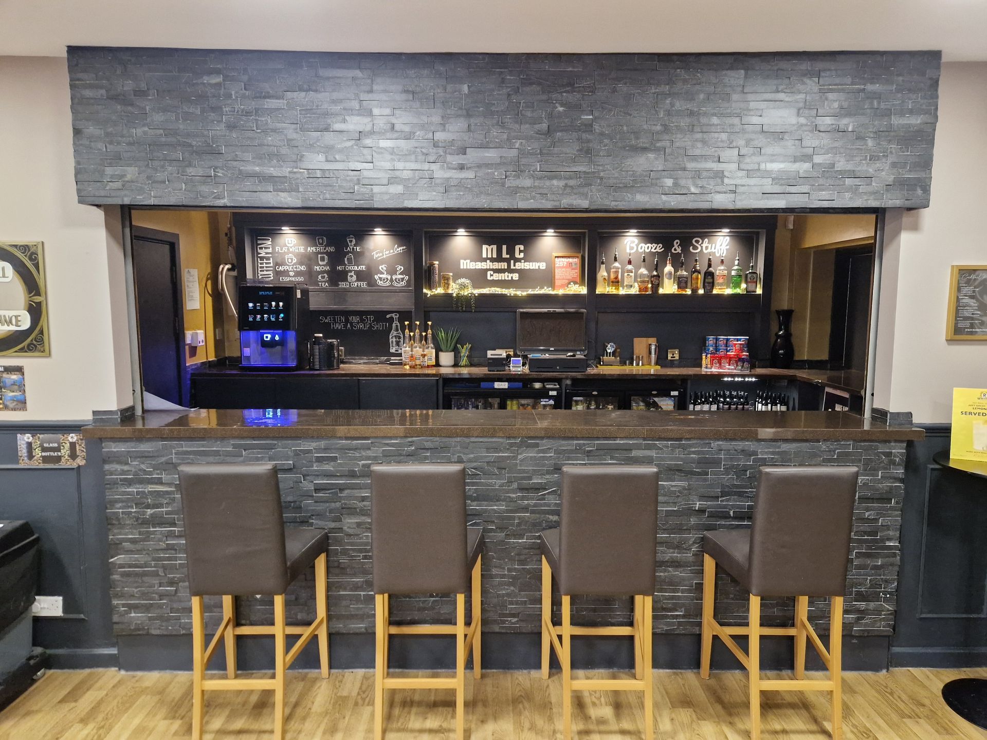 Empty bar with four stools and a gray stone counter in a dimly lit lounge.
